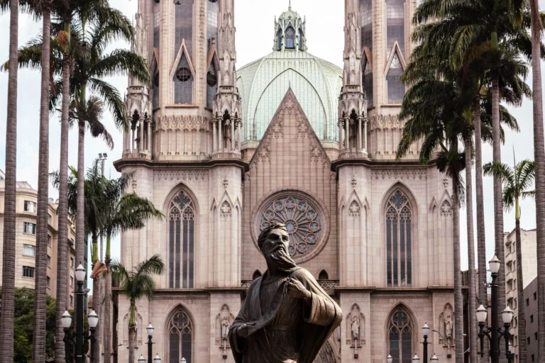 Stunning view of São Paulo Cathedral with towering palm trees and a historic statue in the foreground.