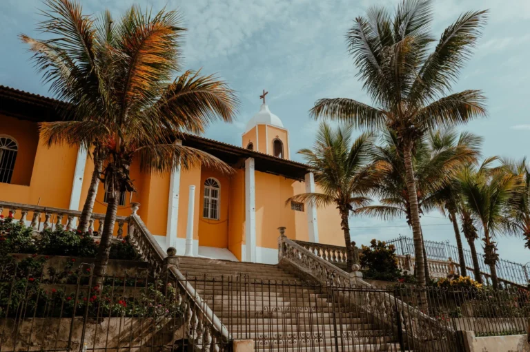 A vibrant church in Pacasmayo, Peru, surrounded by lush palm trees under a clear sky.